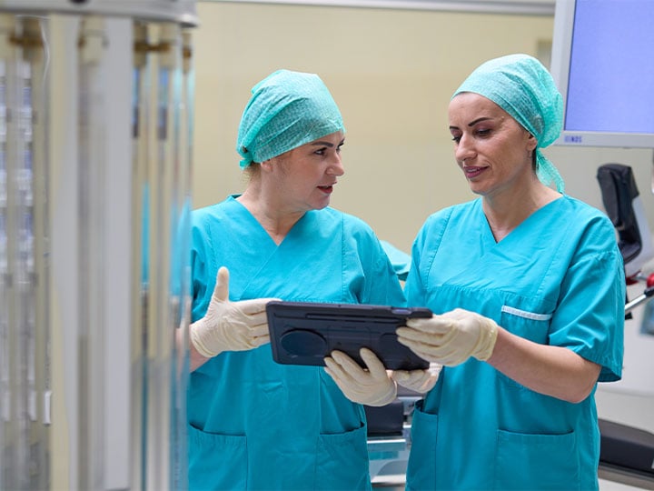 Zwei Frauen in OP-Kleidung unterhalten sich mit einem Tablet in der Hand im Operationssaal.