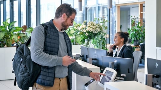 Ein Mann der als Gast zu Sodexo kommt batched sich ein und eine Sodexo Mitarbeiterin ist am Empfang am Telefon