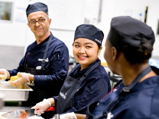 Sodexo Köche sind in ihrer Sodexo Uniform in der Küche und bereiten Gemüse vor
