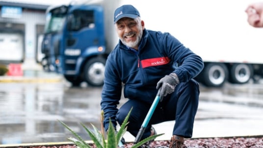 Sodexo Mitarbeitender mit Capi und Sodexo Schriftzug kniet