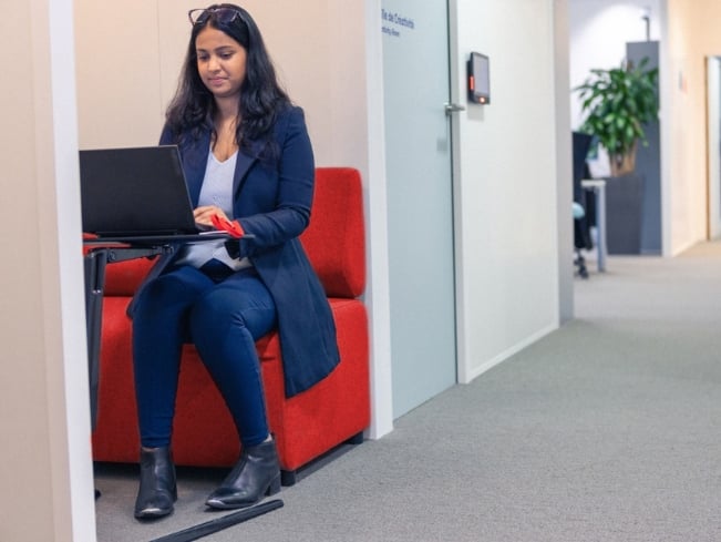 Sodexo Mitarbeiterin arbeitet im einem Booth im Büro am Laptop und fühlt sich sicher und gesund  
