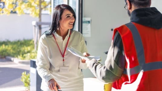 Sodexo Mitarbeiterin uebergibt einem Security mit oranger Weste Dokumente