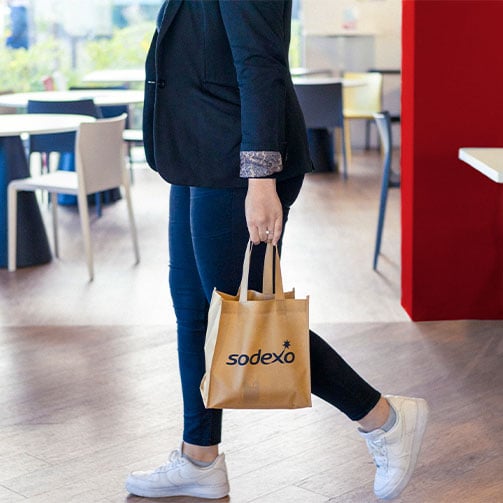 Frau welche in einem Betriebsrestaurant von Sodexo mit einer Sodexo Tüte ist