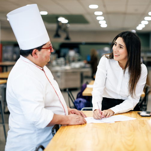 Ein Sodexo Koch und eine Sodexo Mitarbeitende stehen zusammen am Tisch und besprechen den Menuplan.