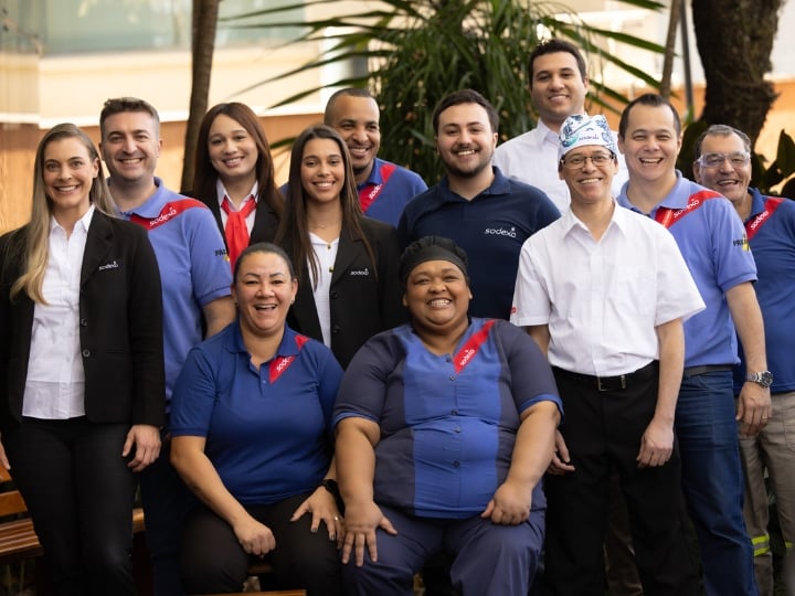 Sodexo Mitarbeitende in ihren Uniformen arbeiten in unterschiedlichsten Jobs und stehen zusammen und lachen.
