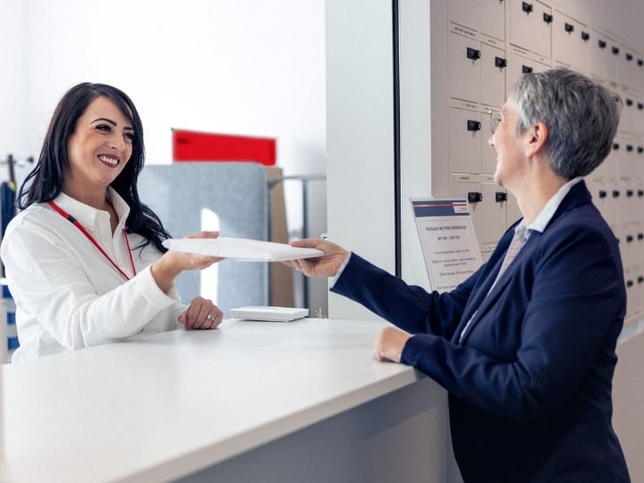 Sodexo Mitarbeiterinnen stehen an einer Theke und die eine Mitarbeiterin gibt der anderen Mitarbeiterin ein Couvert