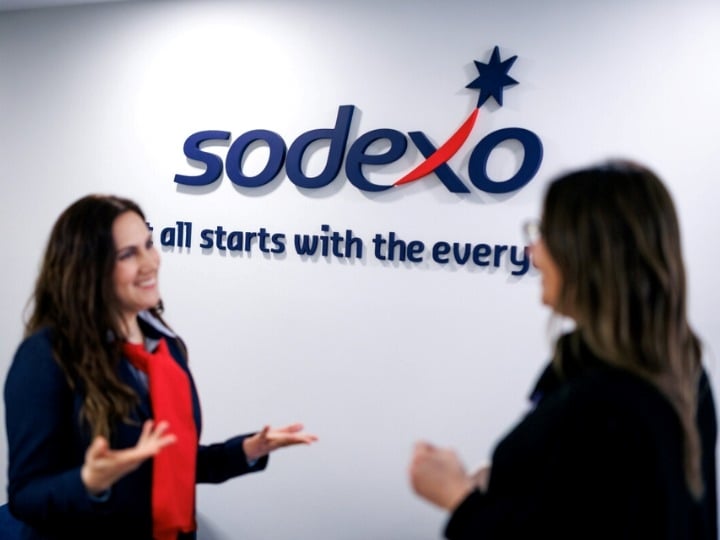 Sodexo Schweiz Mitarbeiterinnen stehen vor dem Sodexo logo und Claim