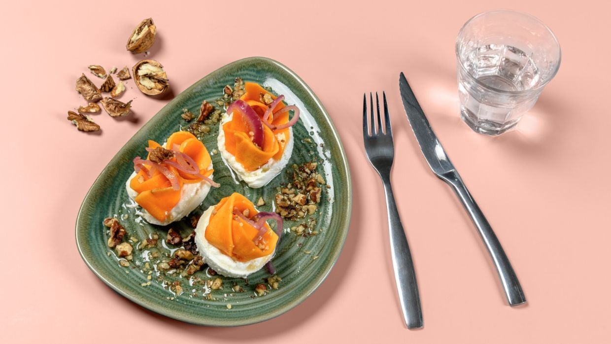 Grüner Teller mit Gericht aus Mozzarella und Pfirsich, Walnuss- und Zwiebel-Topping sowie Besteck als Beispiel für Essverhalten im Arbeitsalltag