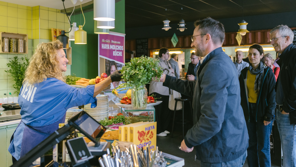 Haya Molcho reicht bei den Sodexo Kochtagen einem Gast einen Teller über die Theke