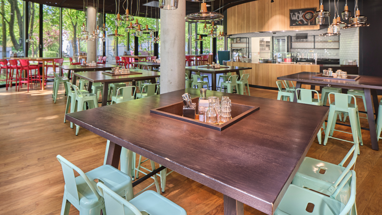 Einblick in das neue Sodexo-Restaurant im arabeska in München mit Blick auf die Tischgruppen und im Hintergrund sieht man die Essensausgabe.