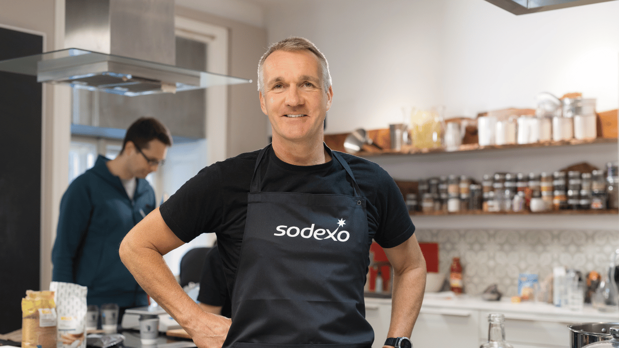 Food-Experte und Rezepte-Entwickler Thomas Hopp von Sodexo posiert in Sodexo-Schürze in einer Küche für die Kamera.