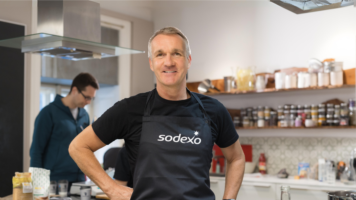 Food-Experte und Rezepte-Entwickler Thomas Hopp von Sodexo posiert in Sodexo-Schürze in einer Küche für die Kamera.