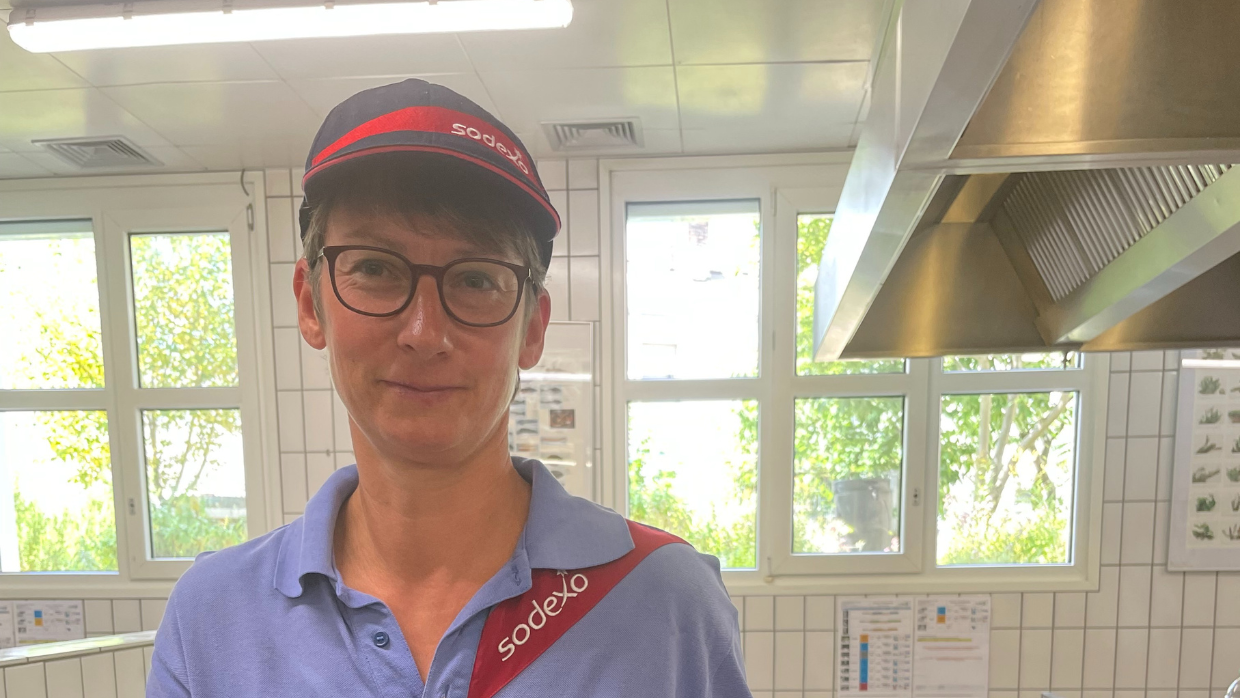 Portrait von Anke Bernhardt, Köchin bei Sodexo, die in einer Großküche ein Gericht präsentiert