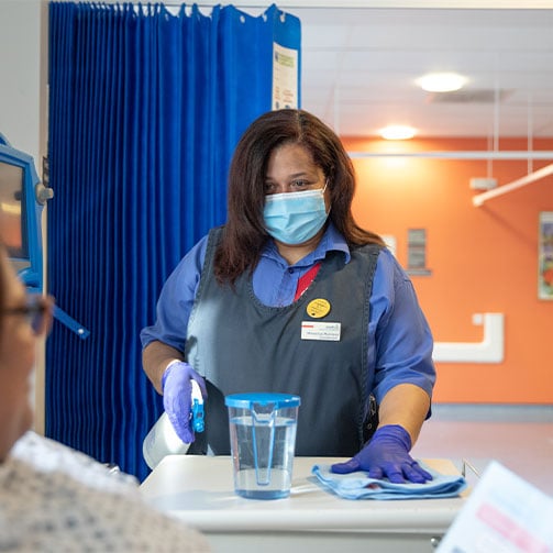 Eine Sodexo-Mitarbeiterin in einer Klinik, ausgestattet mit Maske und Handschuhen, sorgt für Hygiene und Sicherheit.