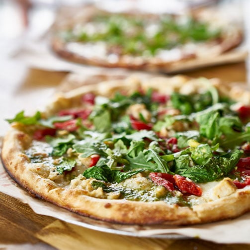 Auf einem Tisch befindet sich eine köstliche Pizza mit Rucola und getrockneten Tomaten, die zum Genießen einlädt.