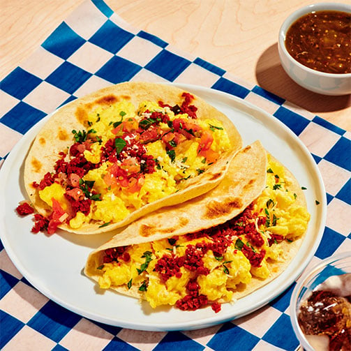 Frühstückstacos: Zwei Tortillas mit pflanzlicher Chorizo und gelbem Rührei auf einem Teller.