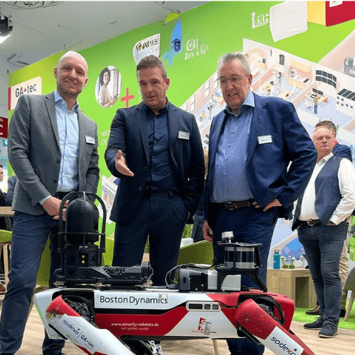 Renato Salvatore, CEO Corporate Services bei Sodexo Deutschland, mit Lars Weide, Head of Sales, und Georg Albrecht, Business Development Director Germany, mit einem Lieferrobotor am Sodexo-Stand auf der Expo Real in München