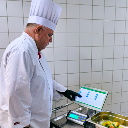 Ein Sodexo-Betriebsleiter in Kochuniform wiegt im Rahmen des „WasteWatch by Leanpath“-Programms Lebensmittelabfälle.