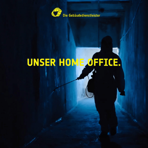 Reinigungkraft in kompletter Schutzmontur desinfiziert einen dunklen Flur. Auf dem Bild steht: Die Gebäudedienstleister und Unser Home Office.
