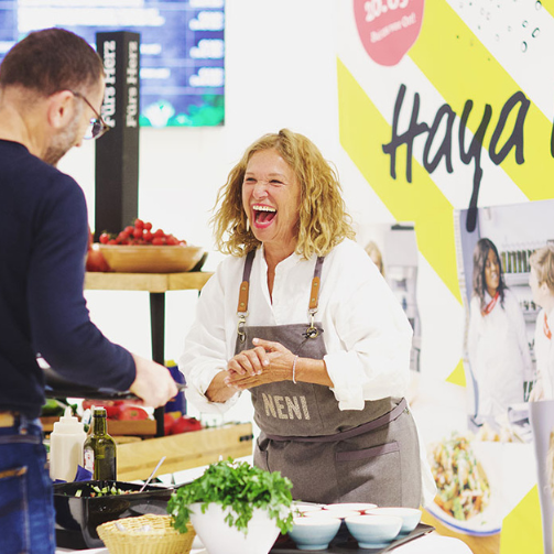 Haya Molcho (Neni) lacht beim Sodexo-Kochevent mit einem männlichen Gast bei der Essensausgabe