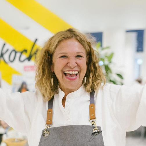 Haya Molcho (Neni) posiert beim Sodexo-Kochevent mit offenen Armen und großem Lachen in einem Betriebsrestaurant.