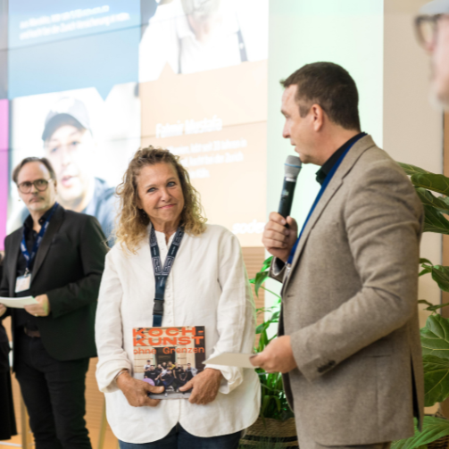 Köchin Haya Molcho und Renato Salvatore, CEO von Sodexo Deutschland, bei der Vorstellung des gemeinsamen Kochbuchs der TV-Köchin und Sodexo. Im Hintergrund steht Michael Wahl, Head of Marketing bei Sodexo Deutschland.