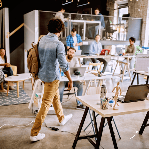 Blick in ein modernes Büro mit Menschen an freistehenden Tischen mit Pflanzen und einem Mezzazin-Bereich.