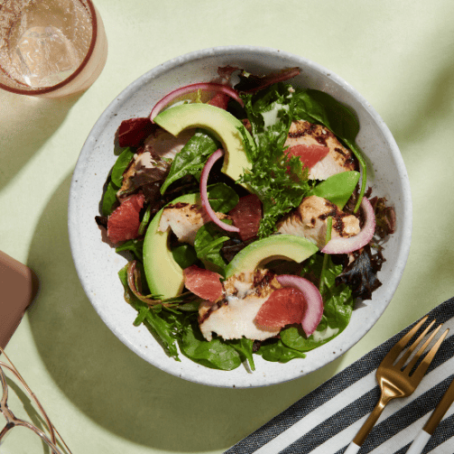 Blick auf einen weißen Teller mit einem Salat mit Avocado, Chicken und Spinat.