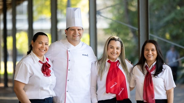 Drei Frauen und ein männlicher Koch in Sodexo-Kleidung stehen nebeneinander und lachen in die Kamera.