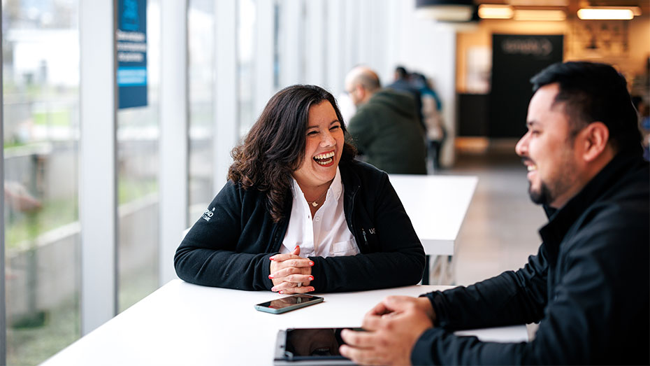 Eine Sodexo-Mitarbeiterin steht mit ihrem Kollegen an einem Stehtisch und unterhält sich lächelnd.