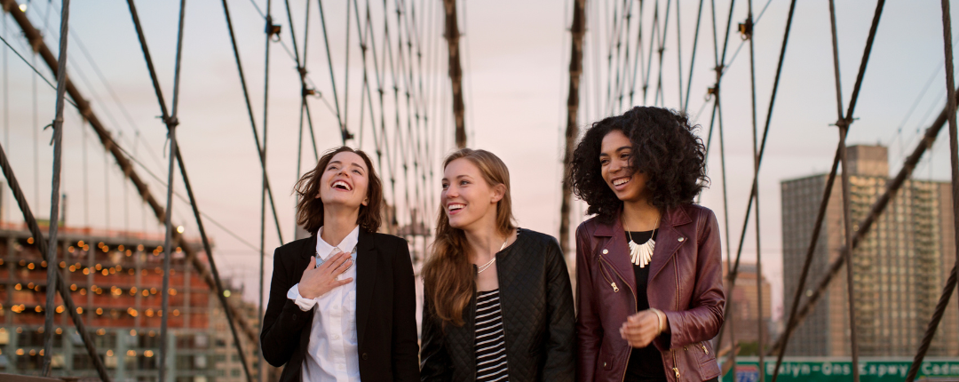 drei junge lachende Frauen auf einer Brücke mit einer Stadt im Hintergrund