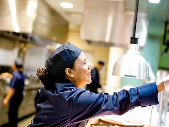 Lächelnde Sodexo-Mitarbeiterin serviert Essen in einer Kantine.