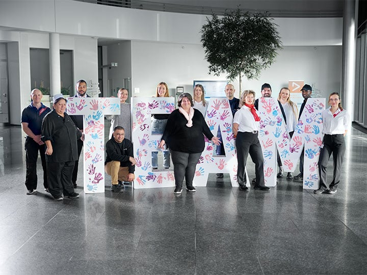 Gruppenbild mit 14 Sodexo-Mitarbeiter:innen im Eingangsbereich eines Kundenstandorts