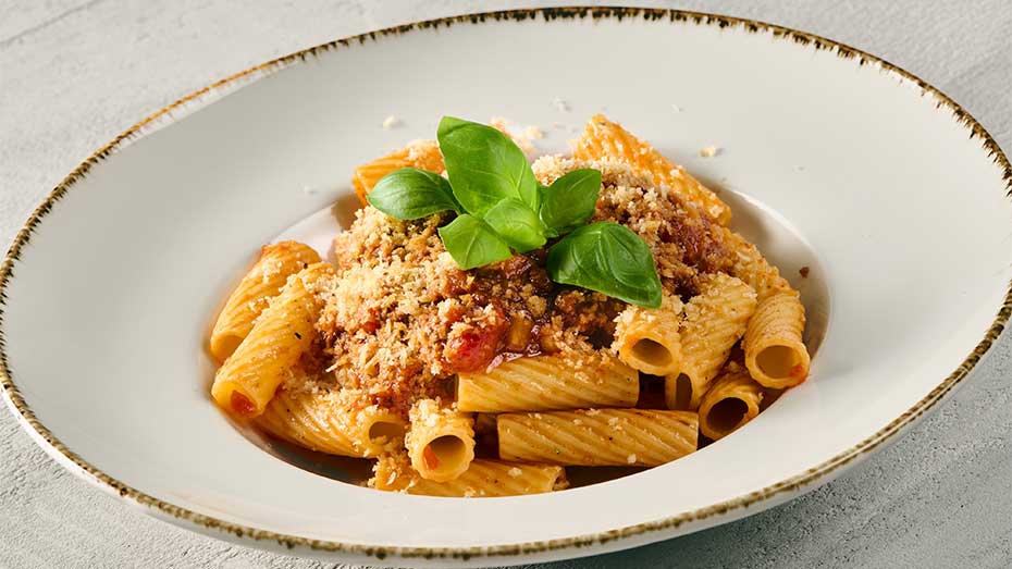 vegane Variante der Spaghetti Bolognese von Sodexo mit Pasta, Tomatensauce, veganem Hack und veganem Parmesan mit Basilikum garniert in einem weißen tiefen Teller.