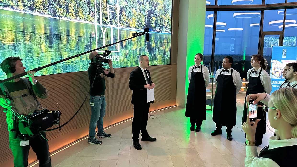 Sodexo Serviceleiter Daniel Löffler weist das Service-Team für eine Veranstaltung vor dem Bildschirm in der Eventlocation Fifity Heights ein.