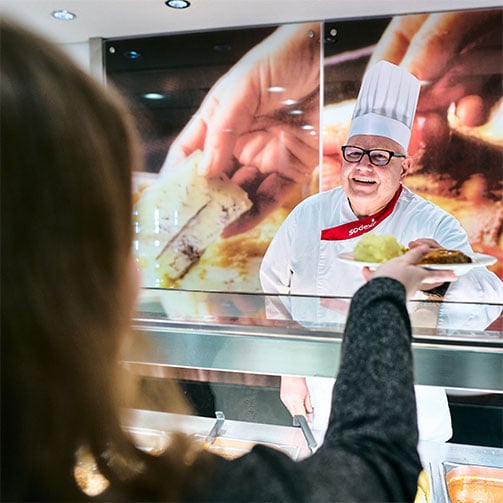 Sodexo-Betriebsleiter Thomas Klatt reicht bei der Essensausgabe einen gefüllten Teller an eine Kundin