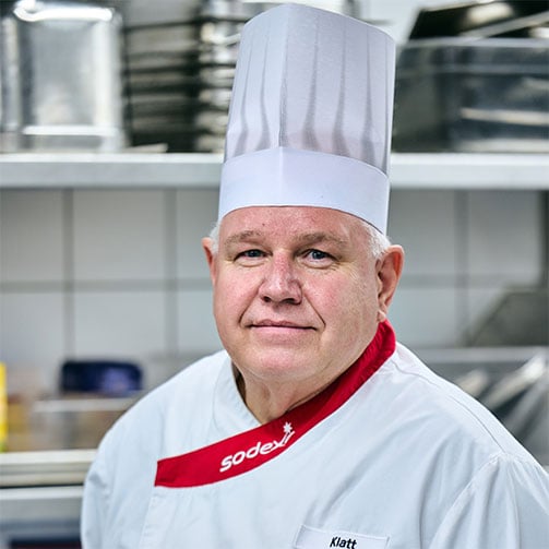 Portrait von Betriebsleiter Thomas Klatt in seiner Sodexo-Kochuniform  in der Betriebsküche