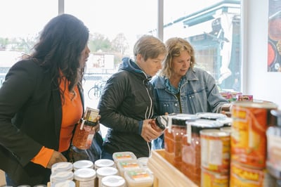 Starköchin Haya Molcho (Neni) und Sodexo-Köchin Anja Rotte sprechen über Produkte in einem Laden des Wiener Naschmarkts. Sodexo-Köchin Catherine Richert steht daneben und hört zu.