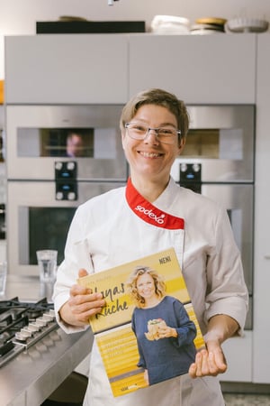Sodexo-Köchin Anja Rotto steht in Küche und präsentiert das Haya Molcho-Kochbuch "Hayas Küche", welches sie von der Starköchin geschenkt bekommen hat.