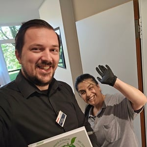 Sodexo Objektleiter Leopold Kolic lachend gemeinsam mit einer Mitarbeiterin, die in die Kamera winkt.