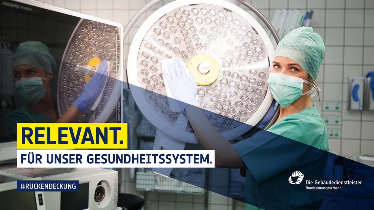 Weibliche Reinigungskraft in OP-Kleidung mit Maske und Handschuhen reinigt Operationsleuchtensystem