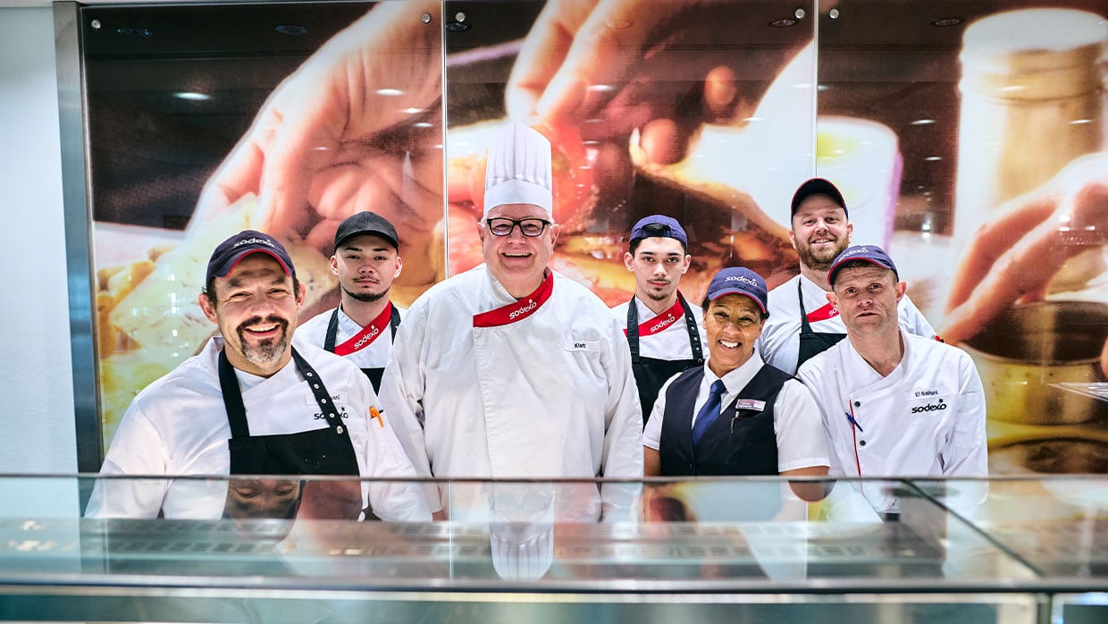 Sodexo-Betriebsleiter Thomas Klatt im Gruppenbild mit einem Teil seines Mitarbeiter-Teams an der Essensausgabe 