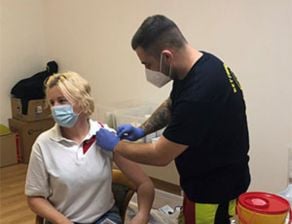 Sodexo-Mitarbeiterin mit Maske erhält gerade sitzend die Corona-Impfung