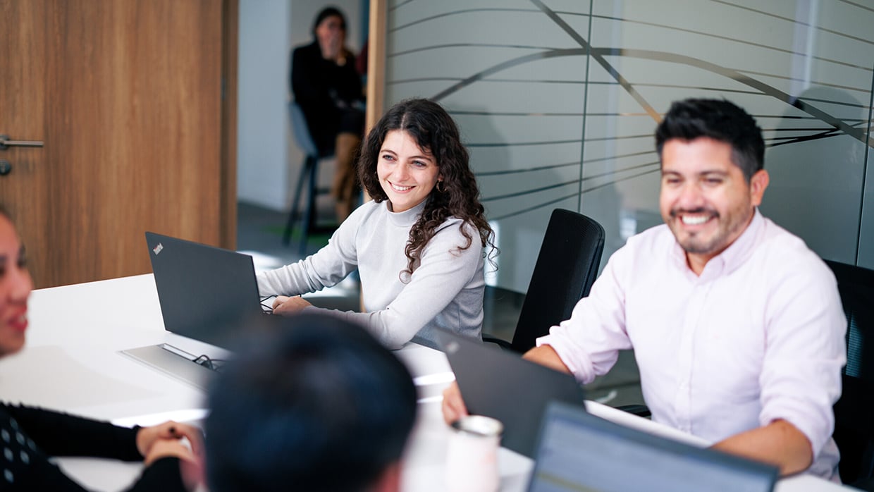 Hymyileviä ihmisiä istuu toimistossa pöydän ääressä