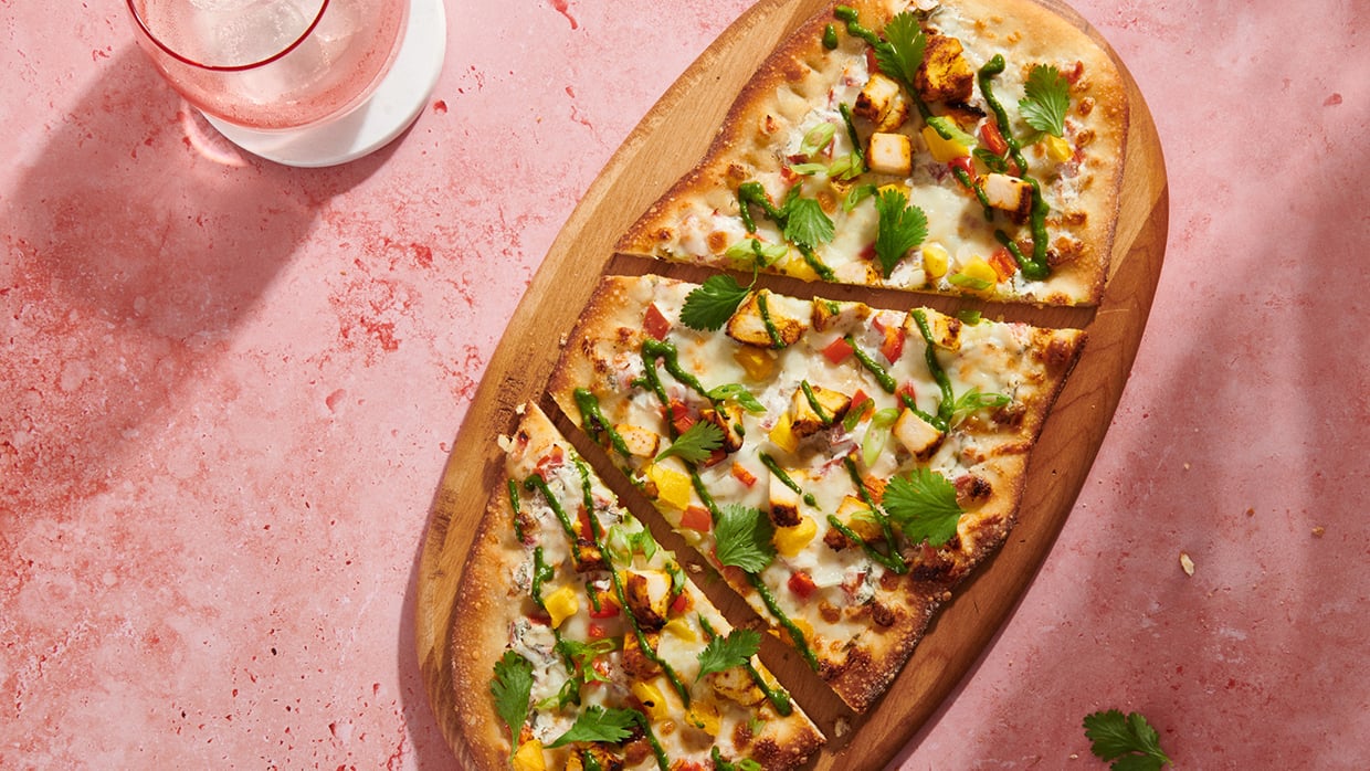 Kuvassa kiviuunipizza tarjottimella ja juomalasi.
