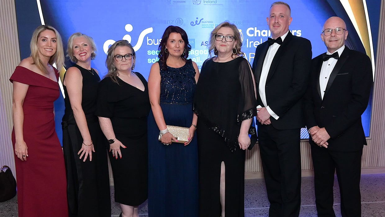 Group of individuals dressed in formal evening wear posing together at an awards event, standing in front of a branded backdrop featuring logos including ‘Chambers Ireland