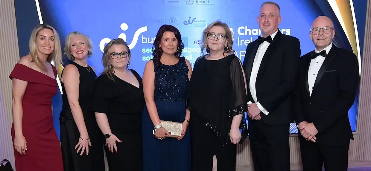Group of individuals dressed in formal evening wear posing together at an awards event, standing in front of a branded backdrop featuring logos including ‘Chambers Ireland