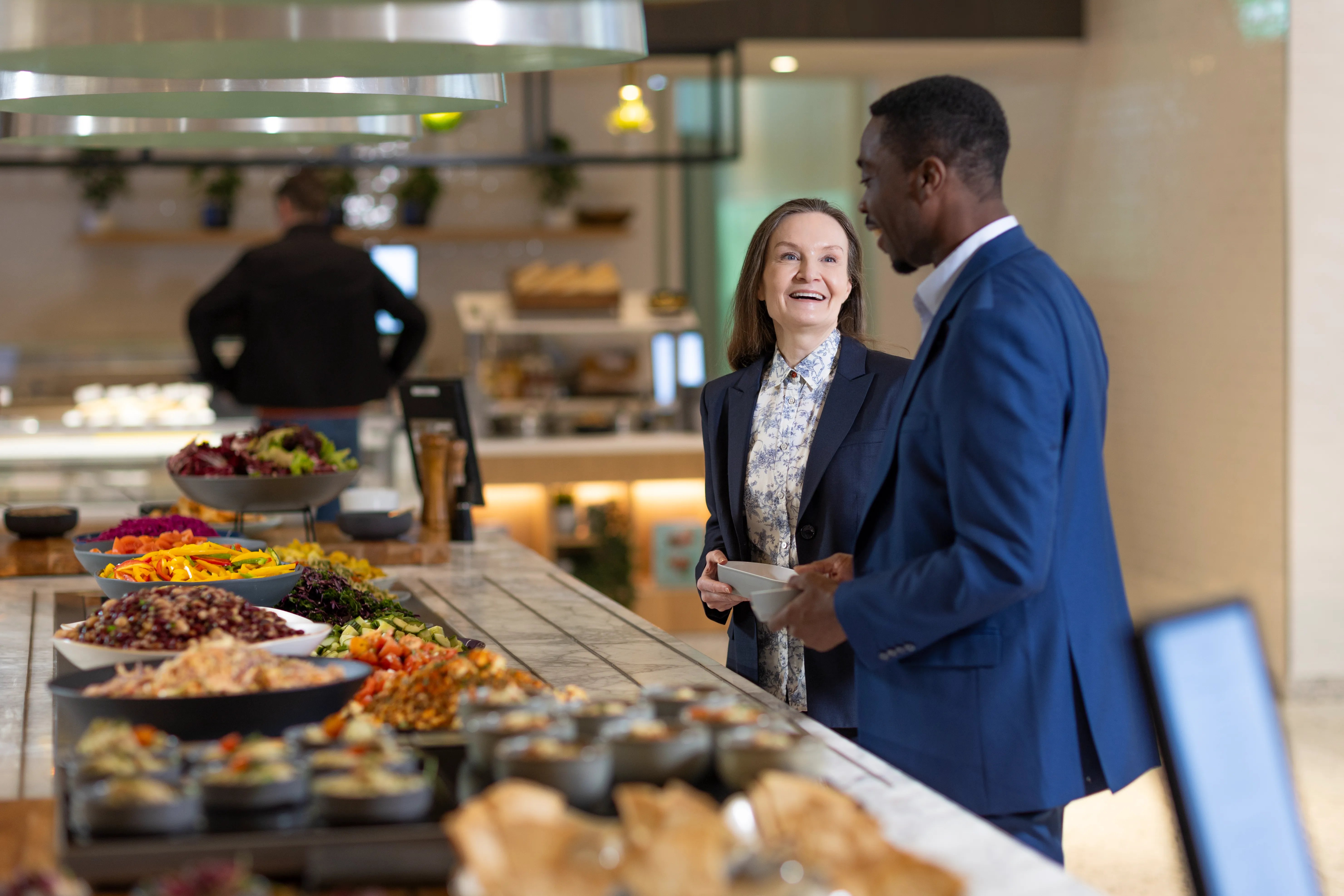 Colleagues selecting freshly prepared food from a healthy workplace dining counter.
