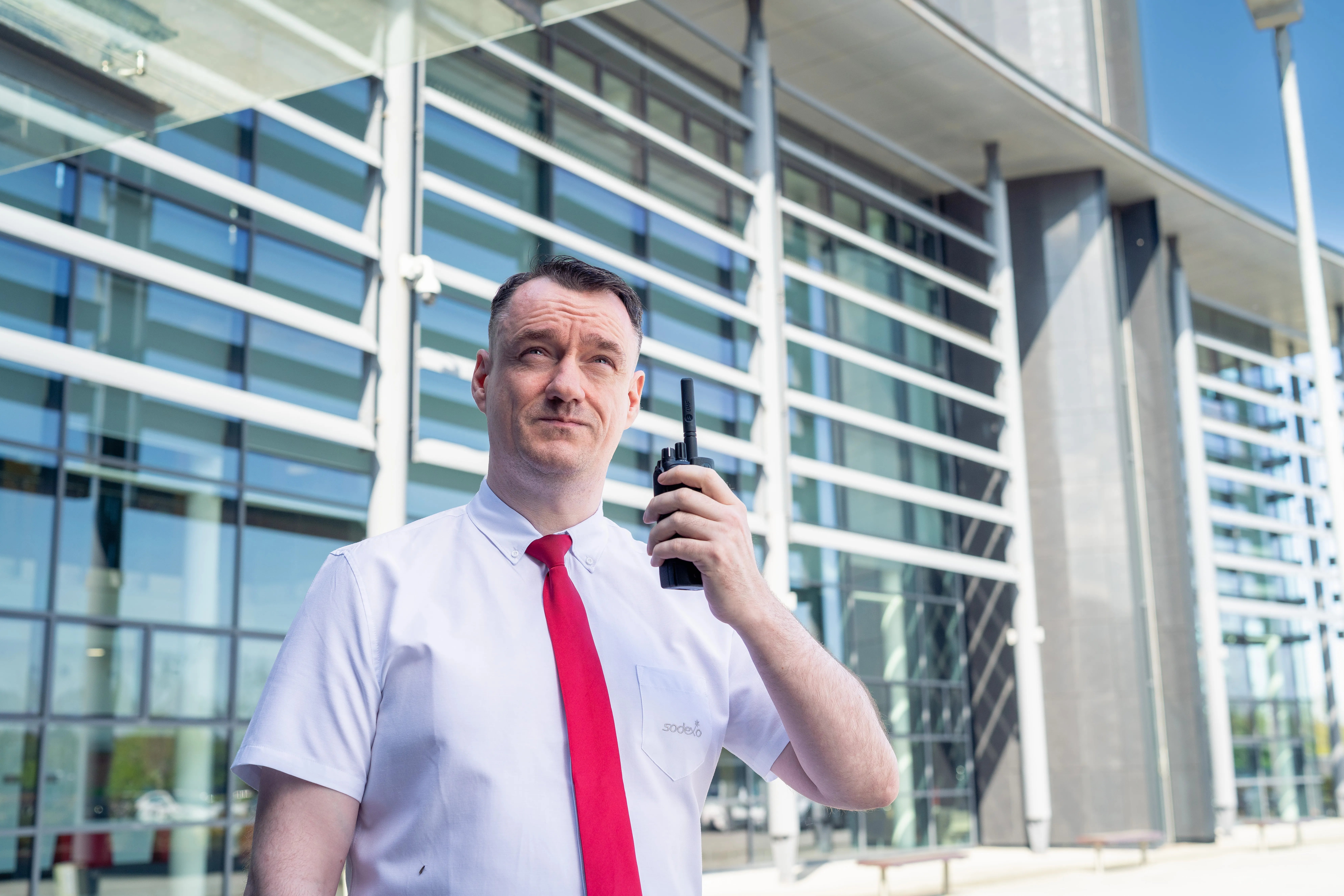 Security officer using a two-way radio outside a modern office building with a glass façade.