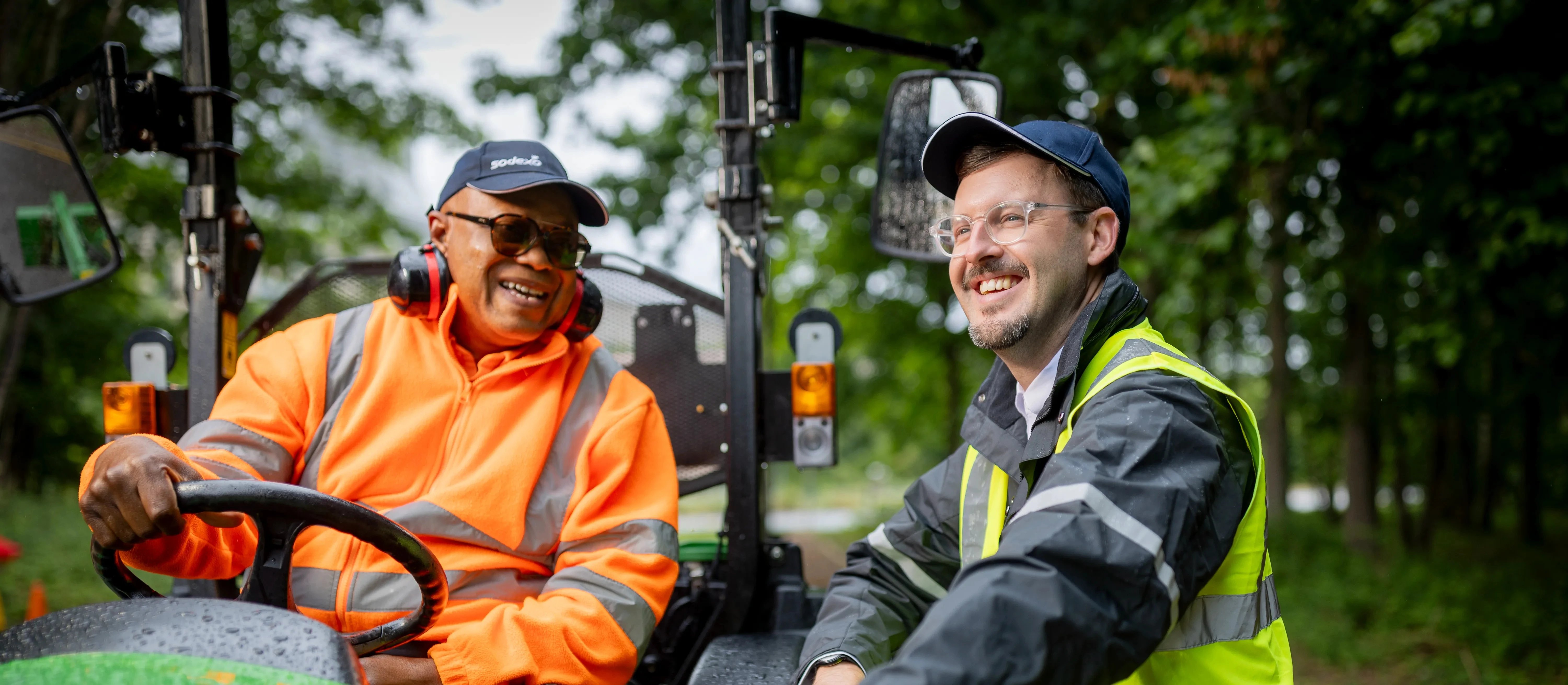 Grounds maintenance team members discussing landscaping work while operating outdoor maintenance equipment in a park setting.